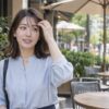 風で乱れた前髪をカフェの入り口で軽く整える女性