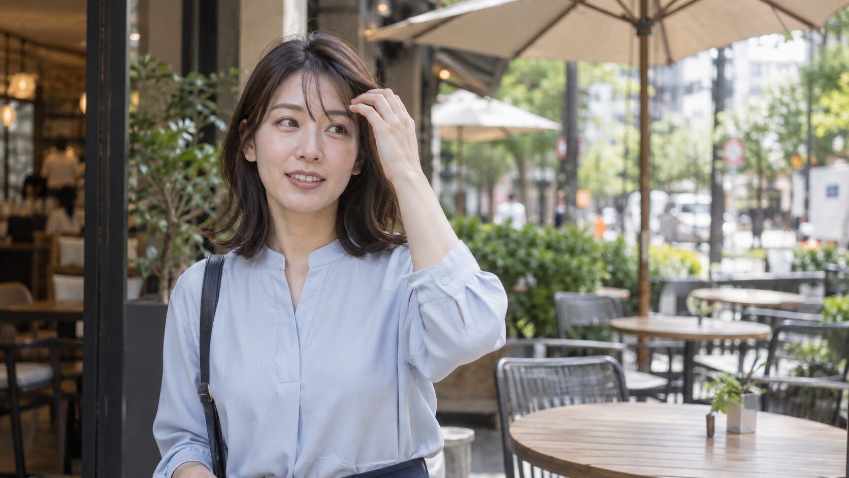 風で乱れた前髪をカフェの入り口で軽く整える女性