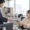 職場のデスクで書類を受け渡す男女