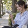 木陰のベンチでスマートフォンのメッセージを見る女性