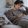 ソファで休みながらスマートフォンを確認する男性
