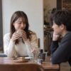 カフェで恋人と向き合い、少し照れながらカップを持つ女性