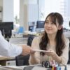 職場で同僚から資料を受け取り、笑顔でお礼を伝える女性