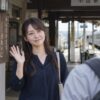 駅前で男性に小さく手を振って別れの挨拶をする女性