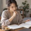 自宅の机で本とノートを見ながら考える女性