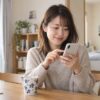 朝のテーブルでスマートフォンのメッセージを考える女性