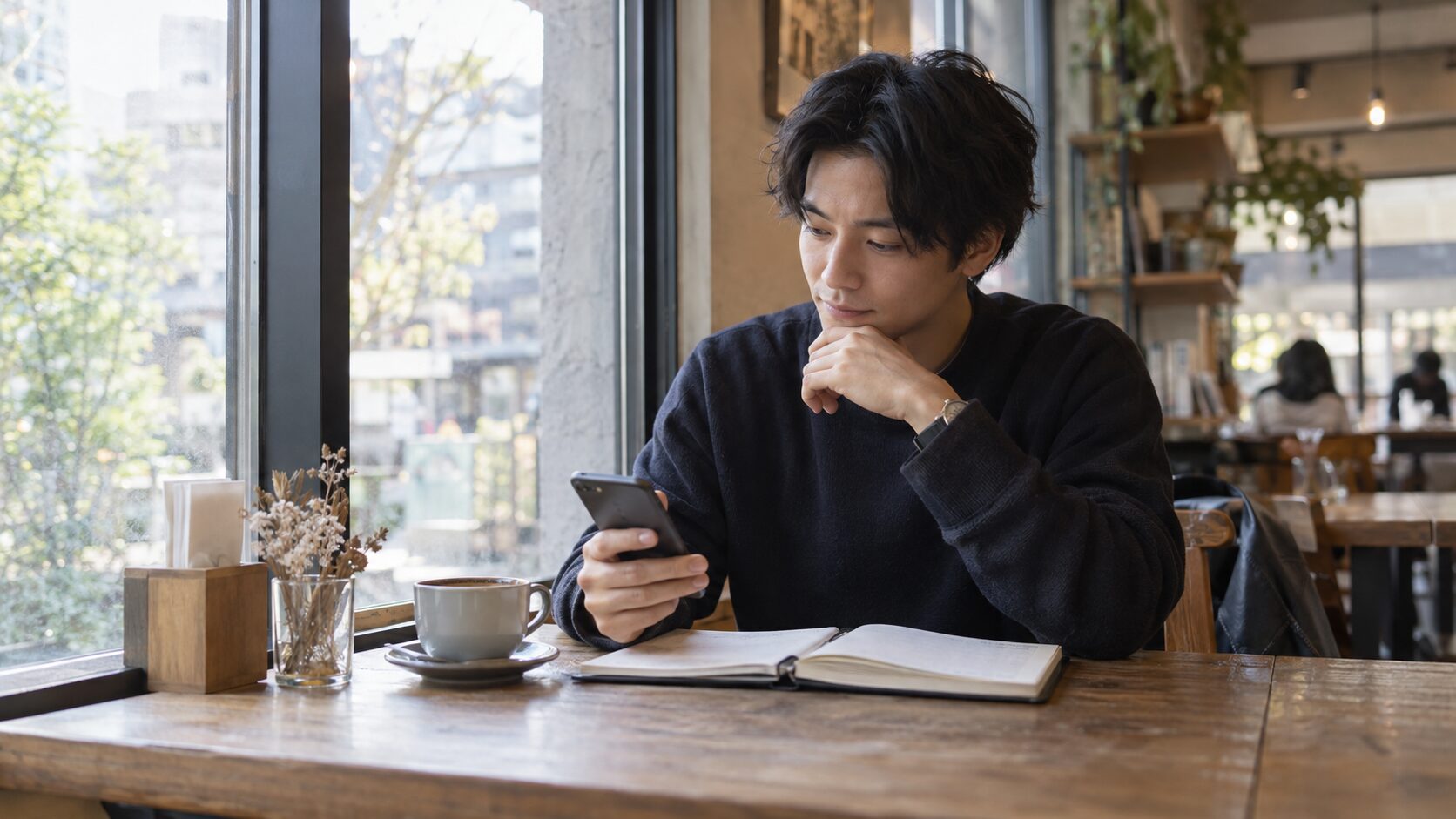 カフェでスマートフォンのメッセージを振り返る男性
